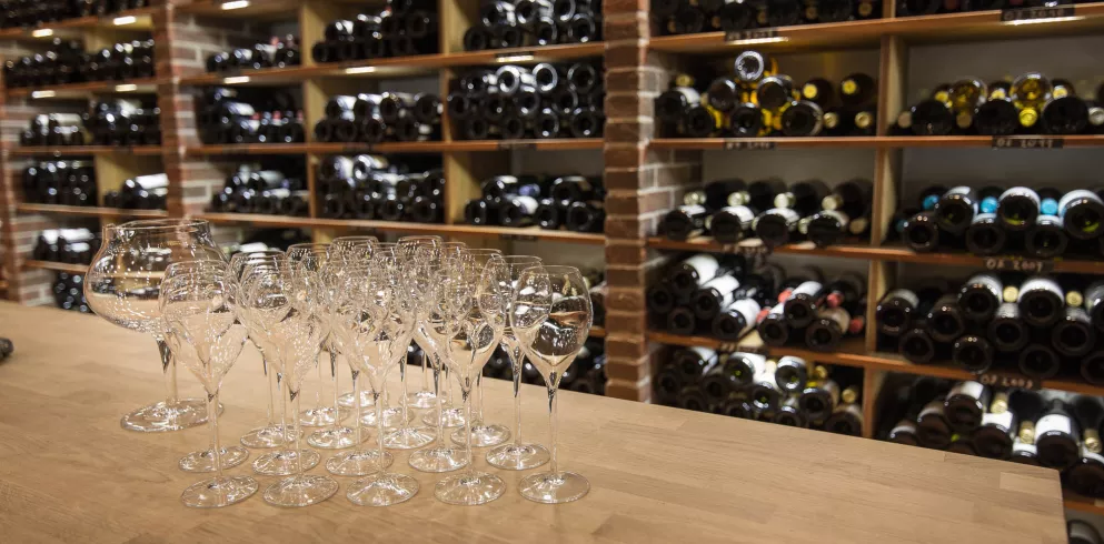 Regale voller Weinflaschen und ein Tisch mit leeren Weingläsern im Weinkeller des Hotel Kunz