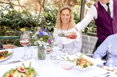 ein schön gedeckter Tisch mit Tellergerichten, Weingläsern und einer Frau, die Wein in ein Glas eingeschenkt bekommt
