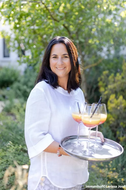 Eine weiß gekleidete Frau mit schwarzen Haaren trägt ein Tablett mit Cocktailgläsern