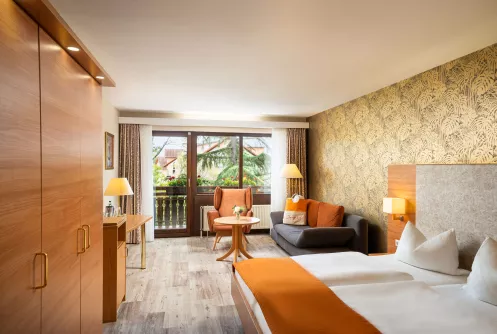 Blick in ein helles Zimmer mit Doppelbett, Holzfußboden, großem Fenster und moderner Tapete