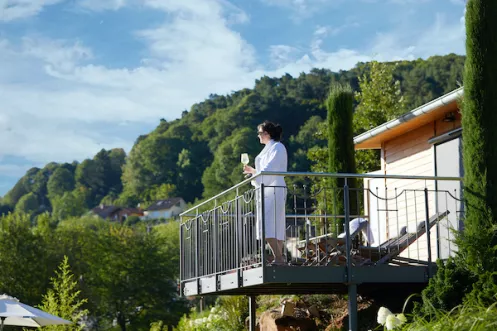 Wiedemanns Weinhotel Ansicht mit Pfälzerwald im Hintergrund und Frau mit Weinglas in der Hand auf Balkon